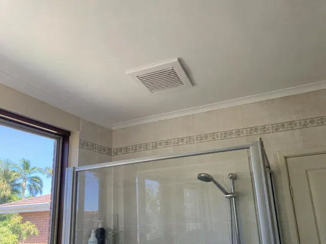 Bathroom ceiling exhaust fan grille above a tiled shower in a light-colored home in Ormeau